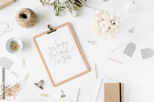 Flat lay, top view office table desk. feminine desk workspace with clipboard and inspirational quote, twine, pencils, floral bouquet, craft diary and clips on white background.