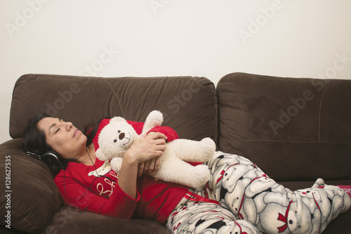 Fototapeta Naklejka Na Ścianę i Meble -  Mujer en pijama durmiendo en sillón con audífonos abrazando oso de peluche