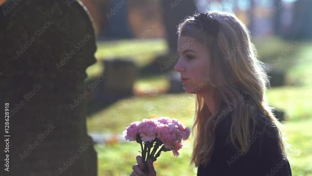 Young girl with bouquet of flowers vising a grave in cemetery.