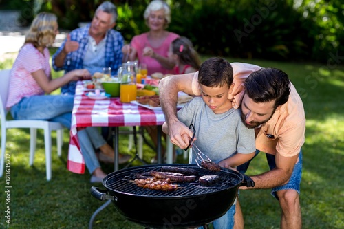 Father teaching son cooking on barbecue with family 