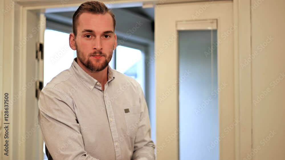A man wearing a shirt, walking in through doors in his home, stopping and looking at camera with a big smile. A man wearing a shirt, walking in through doors in his home, stopping and looking at camera with a big smile.