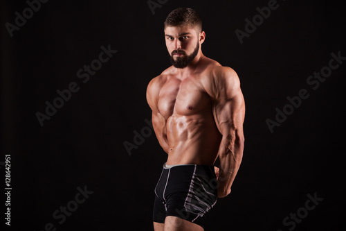 Handsome muscular bodybuilder posing over black background.