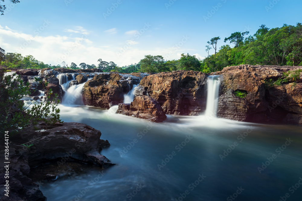 Fototapeta premium Waterfall in forest with blue sky background in long exposure 