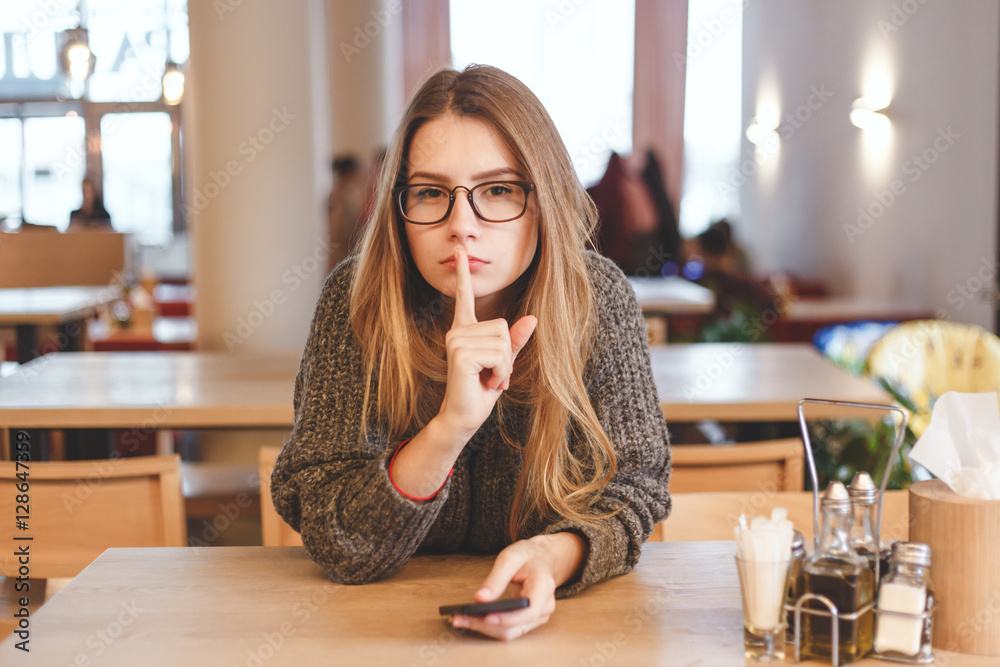 © vladdeep - Young beautiful brunette woman showing silence sign with finger on lips in creative office © vladdeep - Young beautiful brunette woman showing silence sign with finger on lips in creative office