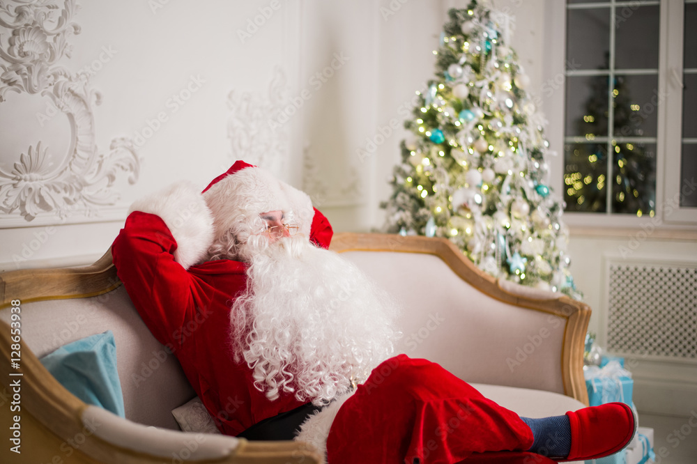 Obraz premium Santa Claus relaxing on sofa against christmas tree at home