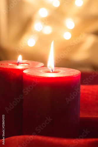 Lit red candles   on red wavy fabric and golden background with bokeh.