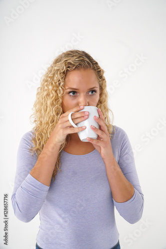 Curly blonde girl drinking tea from a mug. Vertical shot