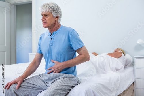 Foto Senior man having stomach pain while sitting on bed