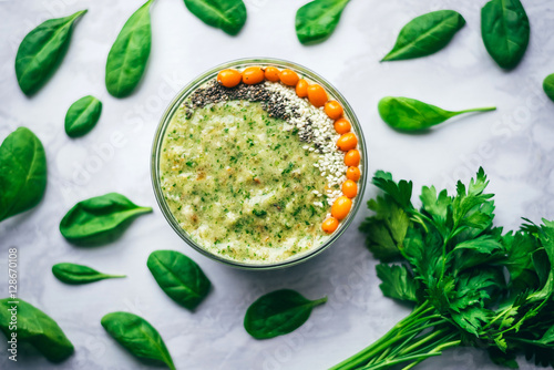 green smoothie with sea buckthorn, Chia seeds and sesame seeds on a white table, around spinach leaves and a bunch of parsley. The concept of healthy eating, vegetarian and vegan food, top view