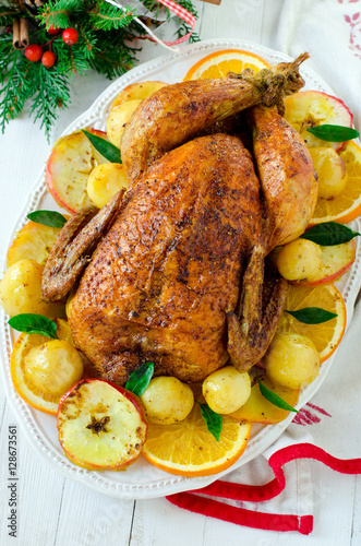 Christmas baked chicken (turkey) with oranges and apples on a wh
