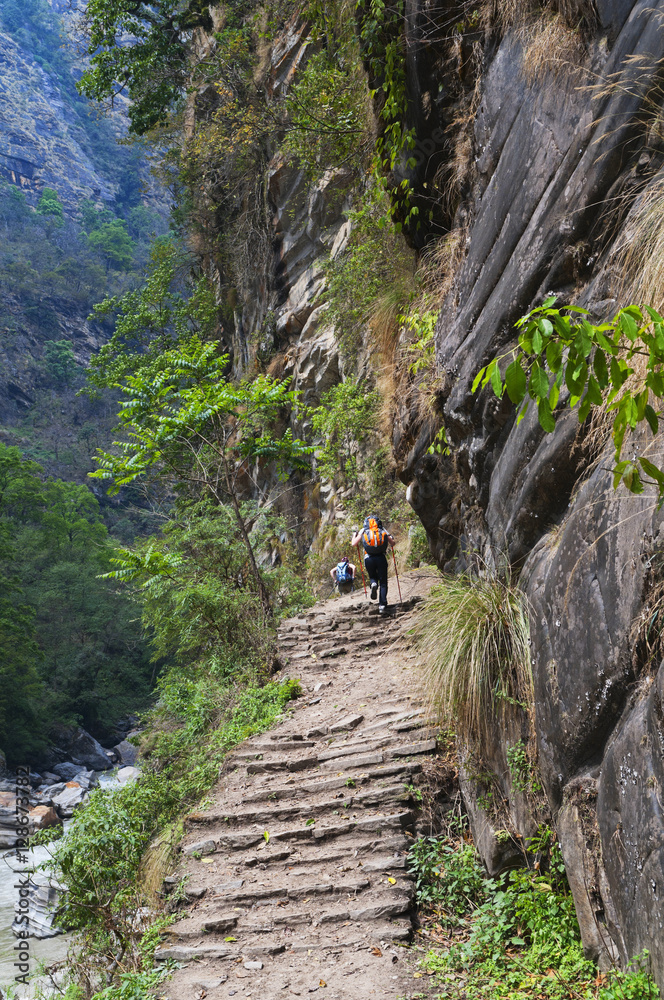 Two climbers on dangerous track with steps from stone rise uphil