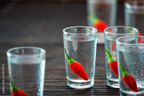 selective focus glasses of cold vodka with chili peppers  on woo