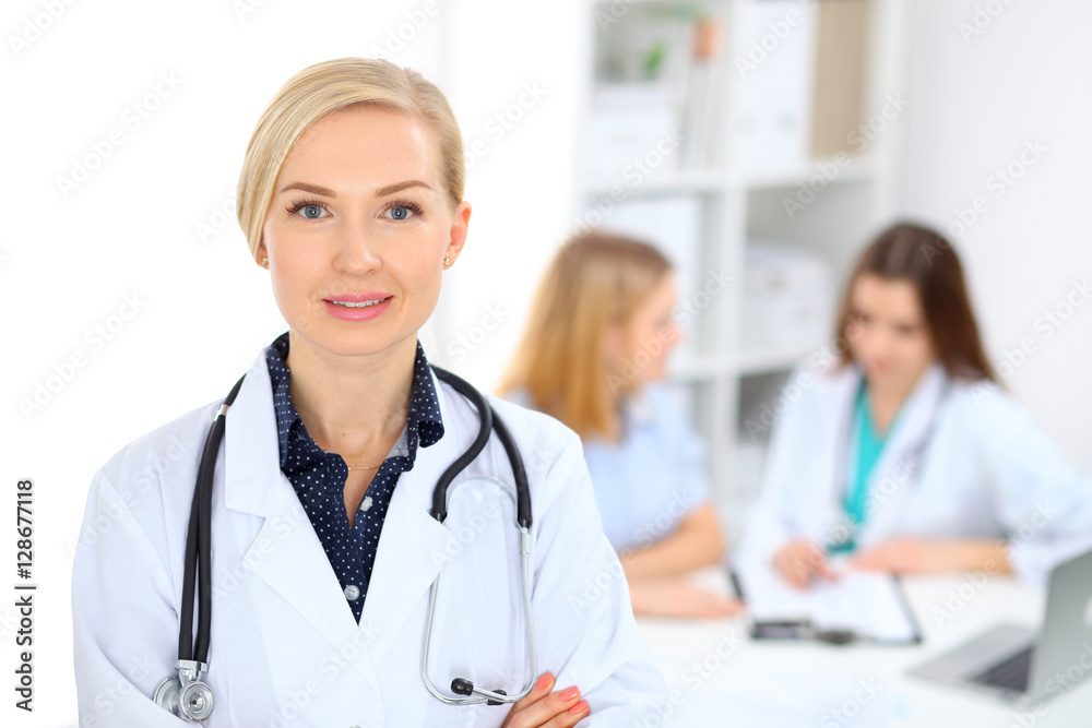 Female doctor smiling on the background with patient and his physician in hospital Female doctor smiling on the background with patient and his physician in hospital