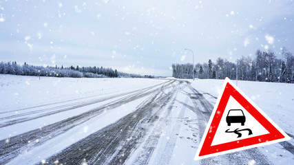Snow covered road, winter driving with road sign - slippery road