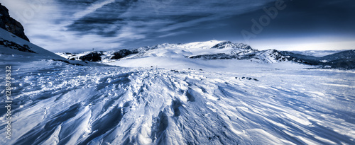 Winter top of the mountains with blue snow windy and scattered clouds no trees