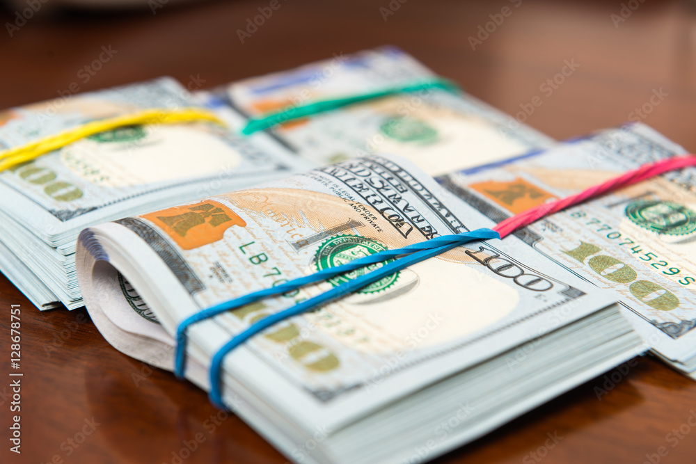 Stashes of hundred dollar bills on wooden table Stashes of hundred dollar bills on wooden table