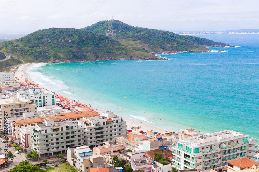 Coastline over paradise beach destination. Hotels, beach umbrellas, and mountains in the background. The water is refreshingly turquoise. Praia dos Anjos in small town Arraial do Cabo in Brazil