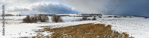 Wide panorama of hilly fields thawed in spring with stormy sky.