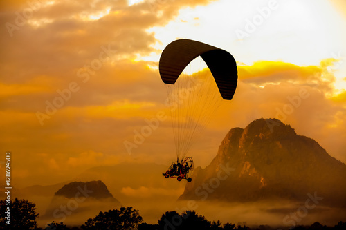 Silhouette paraglider on sunset sky background photo