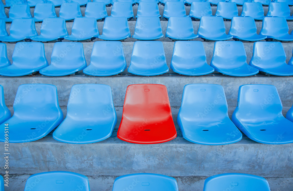 Naklejka premium Single or one red seat or bench in the middle or center of blue chair in the football or soccer stadium.