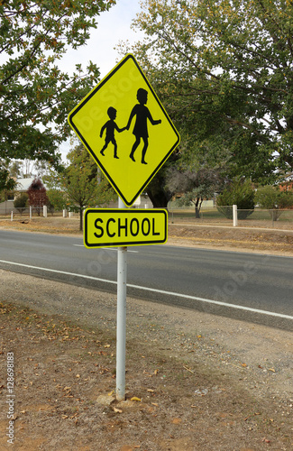 black and yellow School sign with fenced schoolground in background photo