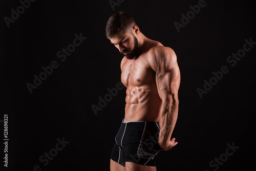 Handsome muscular bodybuilder posing over black background.