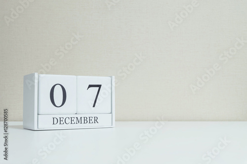 Closeup white wooden calendar with black 7 december word on blurred white wood desk and cream color wallpaper in room textured background with copy space , selective focus at the calendar