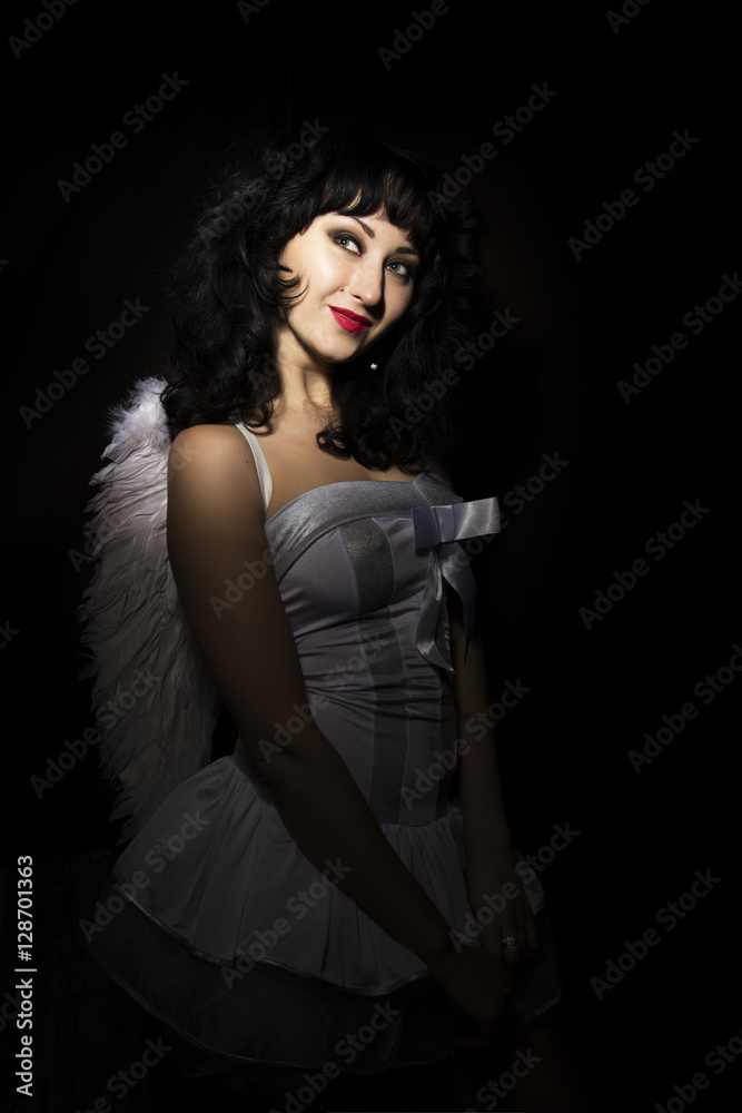 Beautiful bride wearing white dress with professional make-up and hairstyle, wings behind. on a dark background