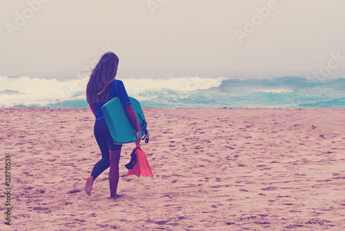 girl with  board goes on the bank of ocean.