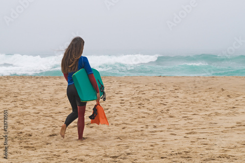 girl with  board goes on the bank of ocean.