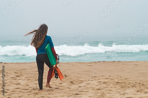 girl with a board goes on the bank of ocean.