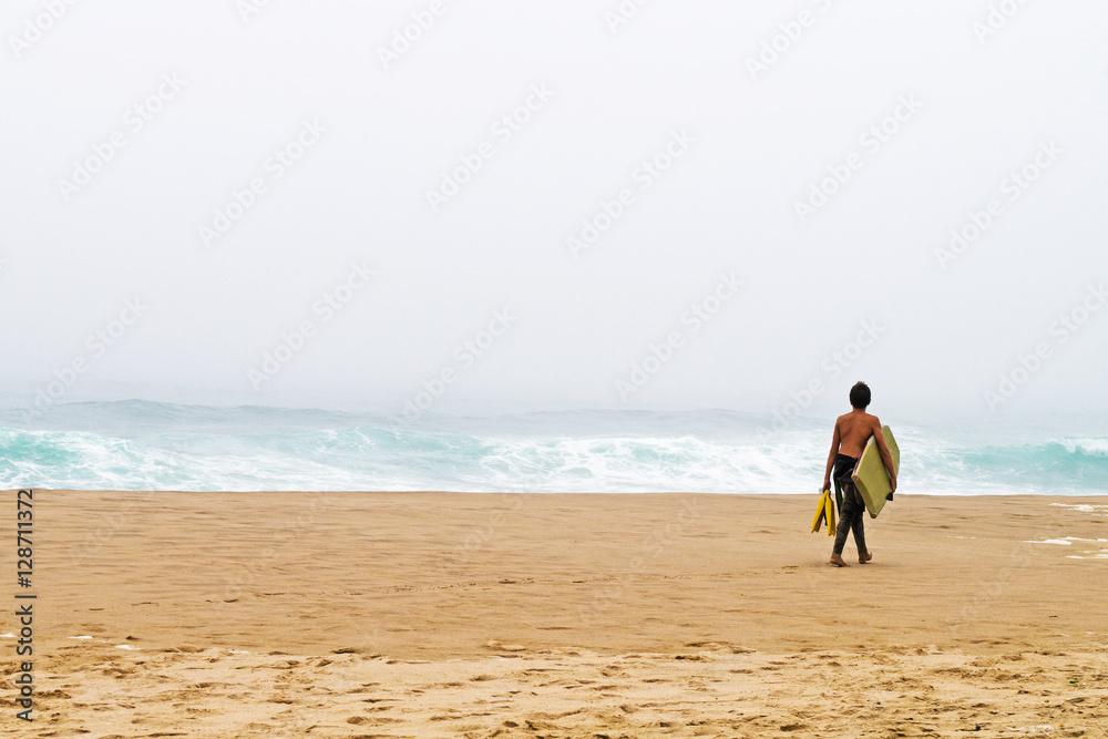 young surfer with  board goes on the bank of ocean.