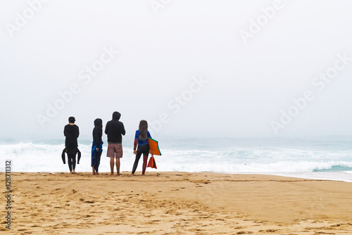 Four surfers stand ashore ocean.