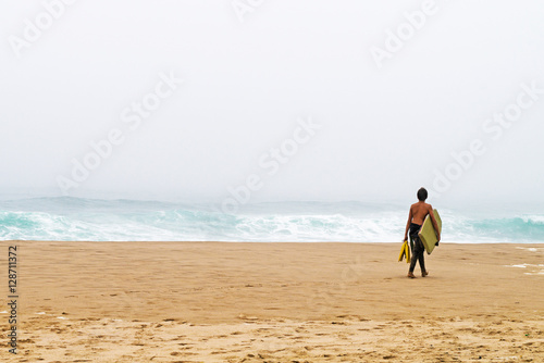 young surfer with  board goes on the bank of ocean. © JULIA LARINA