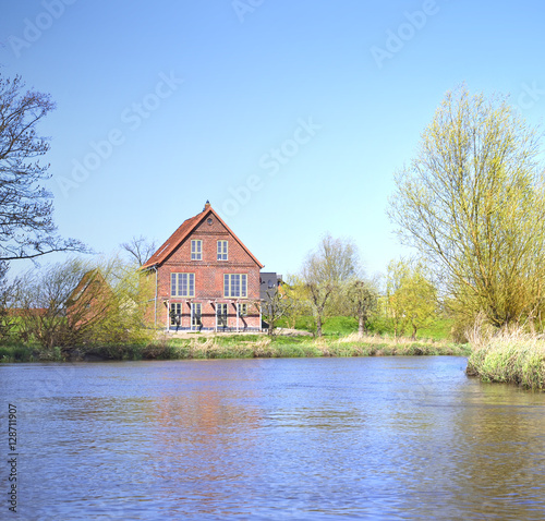 Idyllic river scene with old house and blue sky, spring scene.