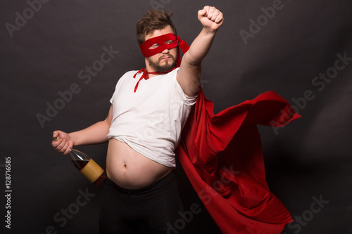 Quadro su tela Bad super hero man in red mask holding bottle of wine or whiskey in studio