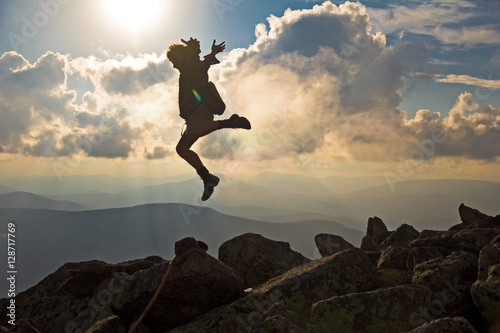 Hiker with backpack jumping over rocks sunset sky on the background