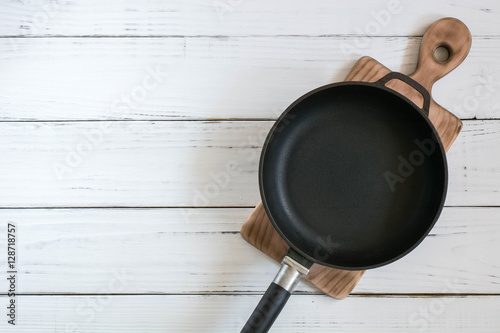 Old cast frying pan and cutting board are on the painted white wooden table