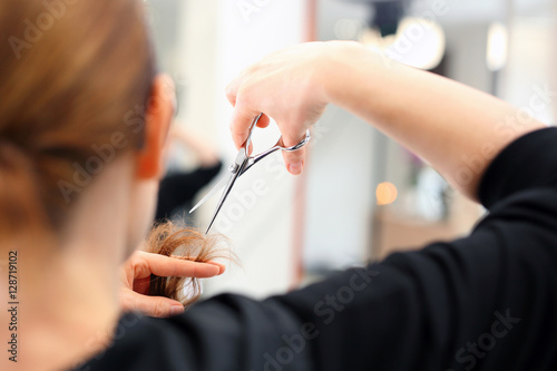 Podcinanie rozdwojonych końcówek włosów.
Fryzjer strzyże kobietę w salonie fryzjerskim
