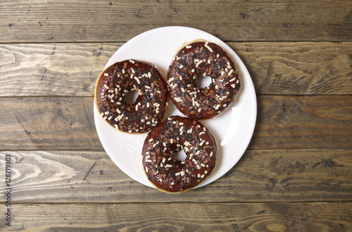 Aerial view of a plate of iced chocolate sprinkle ring donuts on a rustic wooden table background