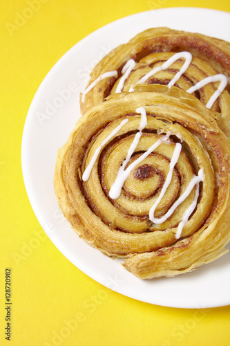 A close up of a plate of freshly baked cinnamon swirls on a bright yellow background