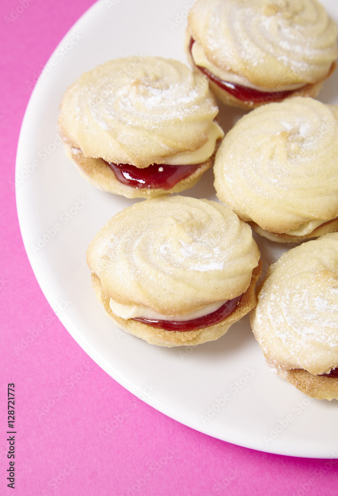A close up of a plate full of freshly baked Viennese whirl biscuits on a bright pink background