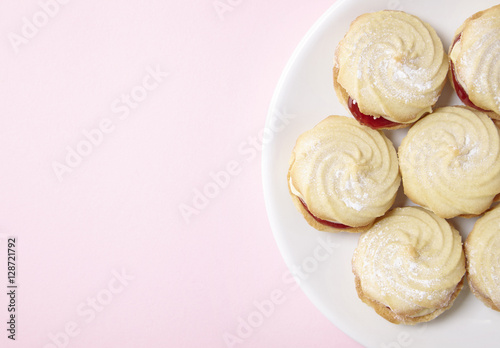 Aerial view of a plate full of freshly baked Viennese whirl biscuits on a pastel pink background with empty space at side
