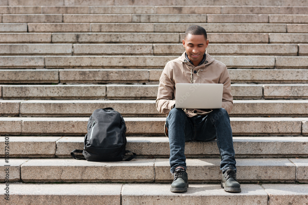 Happy african man sitting on staircase while using laptop