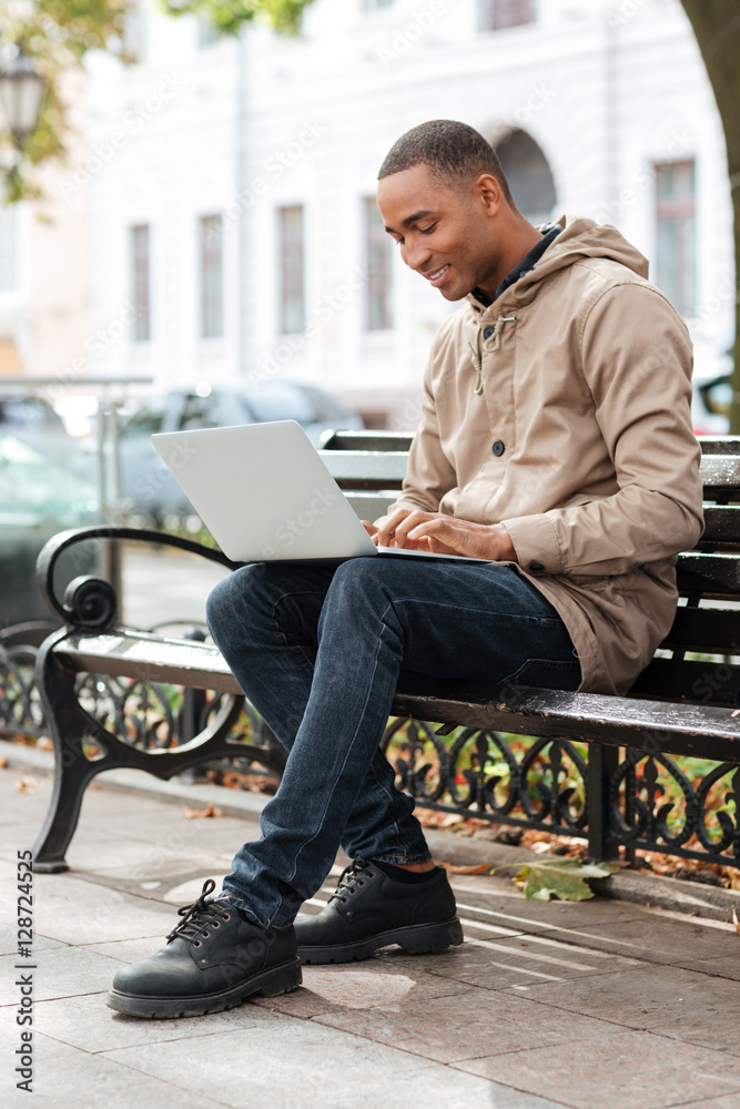 Young man with laptop sitting on wooden bench and typing