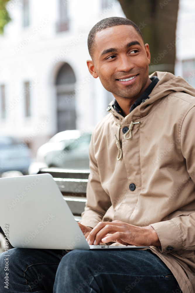 Young african man with laptop sitting on bench and typing Young african man with laptop sitting on bench and typing