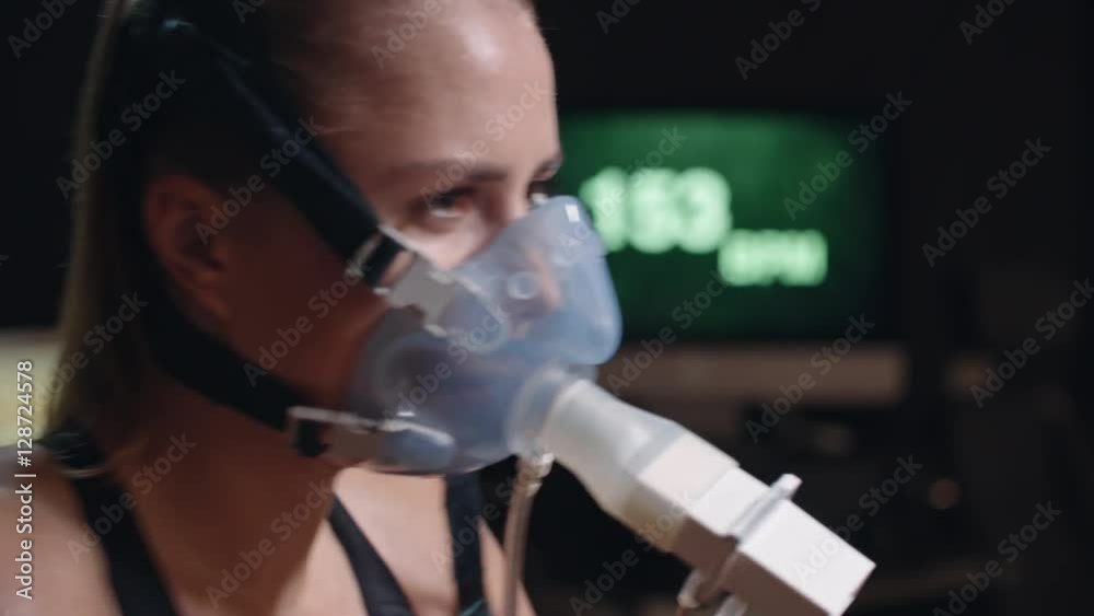 Rack focus from display with heart rate to face of exhausted female athlete in oxygen mask cycling exercise bike