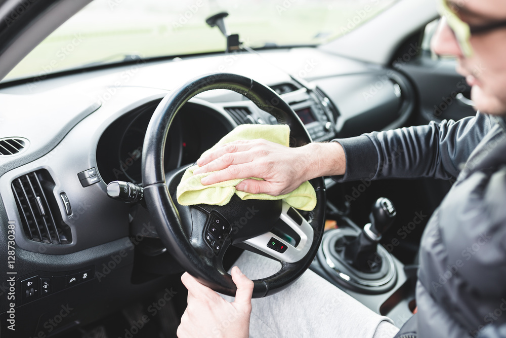 Mature male with glasses cleaning car dashboard with a yellow cloth.