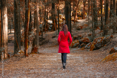 Foto Young woman walking away alone on a forest path wearing a red overcoat