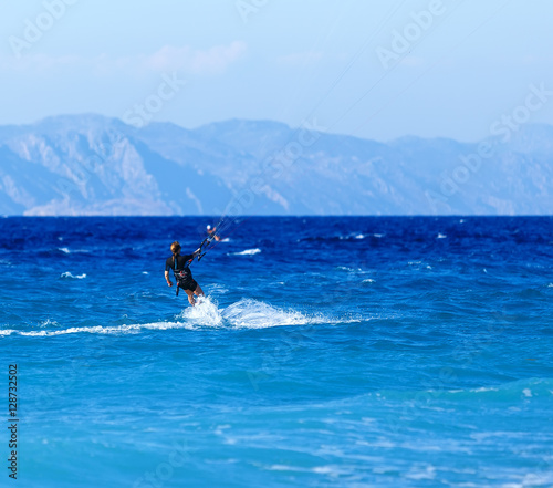 young woman kite-surfer rides in greenish-blue sea under clear skies